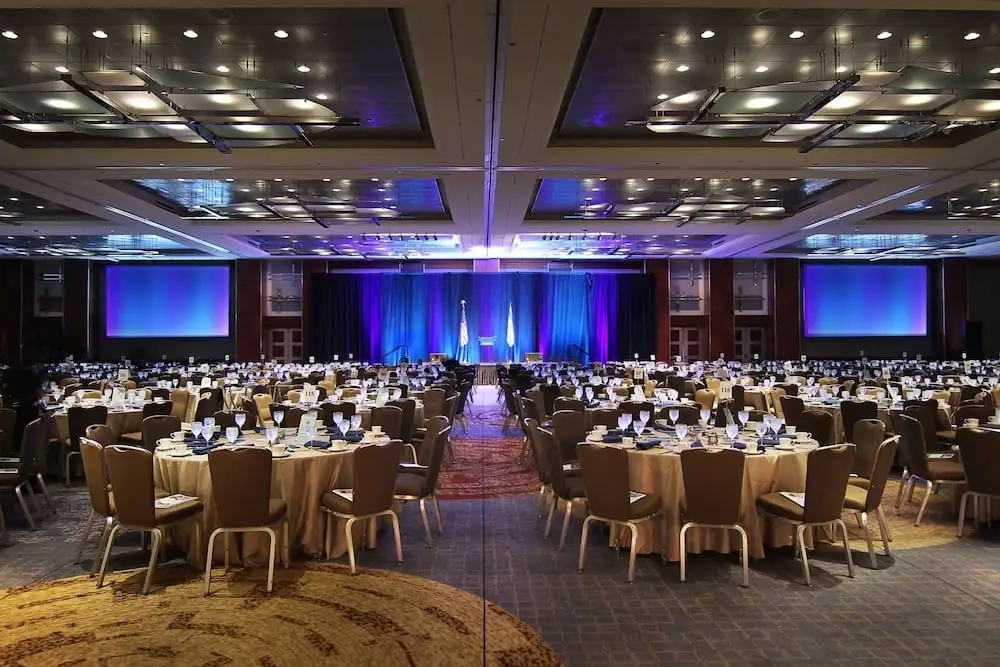 A Hyatt Regency Chicago banquet hall set up for a conference - hundreds of round tables, a stage with a podium, and large screens with blue lighting